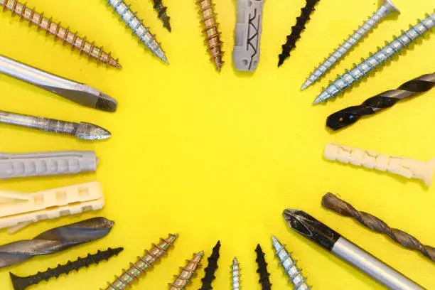 Varios tornillos metálicos y taquetes organizados sobre superficie amarilla, herramientas esenciales, Cómo Instalar un Taquete en un Muro de Block Hueco.
