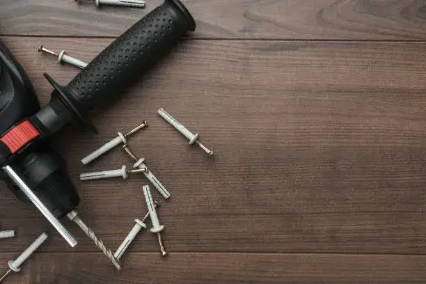 Taquetes de plástico junto con tornillos metálicos y un taladro sobre mesa de madera, herramientas básicas, ¿Qué sistema de fijación necesito para concreto?